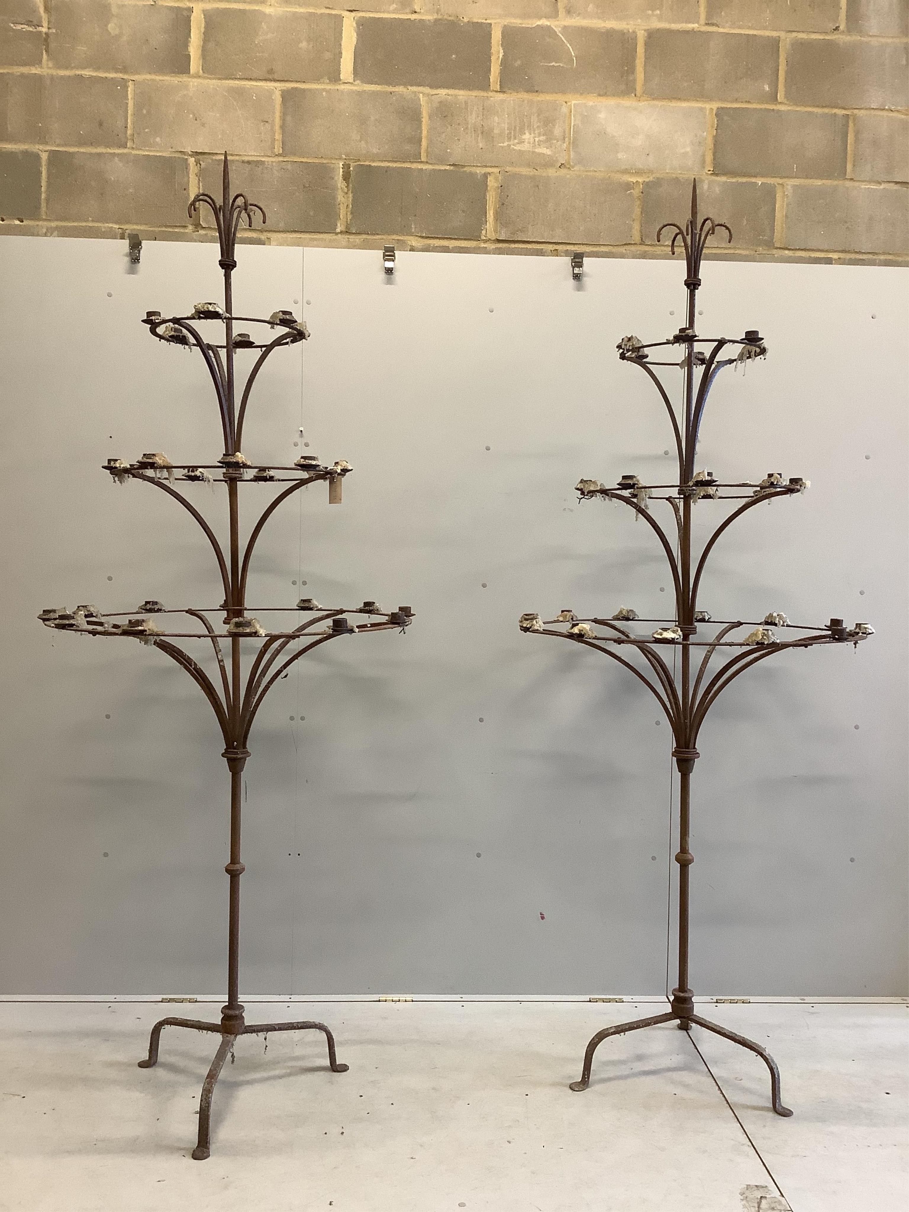 A pair of French wrought iron three tier candlestands, on tripod bases, diameter 95cm, height 254cm. Condition - fair although rusted